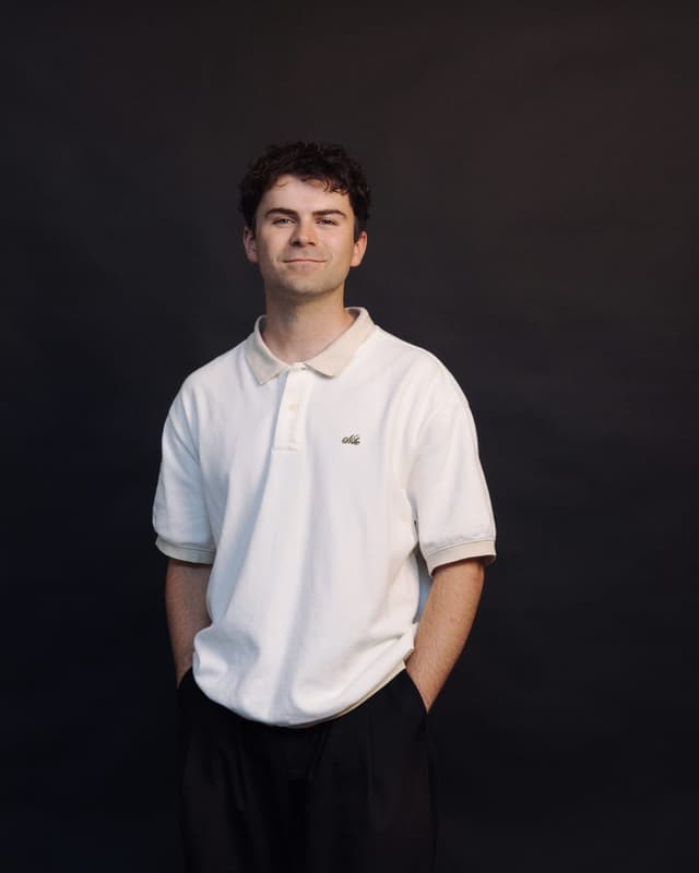 A studio portrait of a smiling man in a white polo shirt against a dark backdrop.