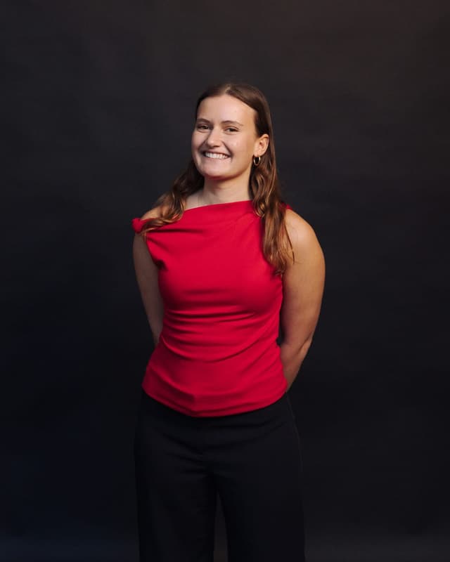 A woman in a red top smiles for a studio portrait against a dark background.