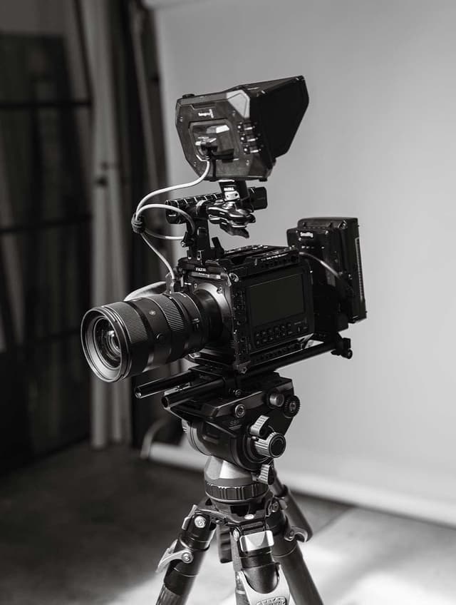 A black and white cinema camera rig mounted on a tripod in a studio.