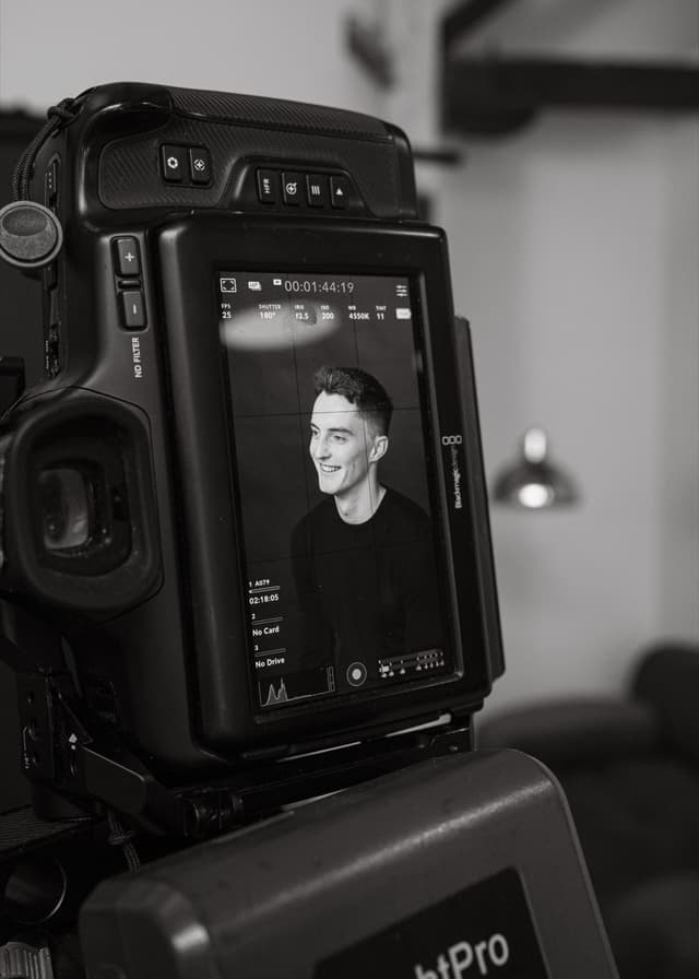 A black and white camera monitor displays a smiling man's portrait during a studio video shoot.