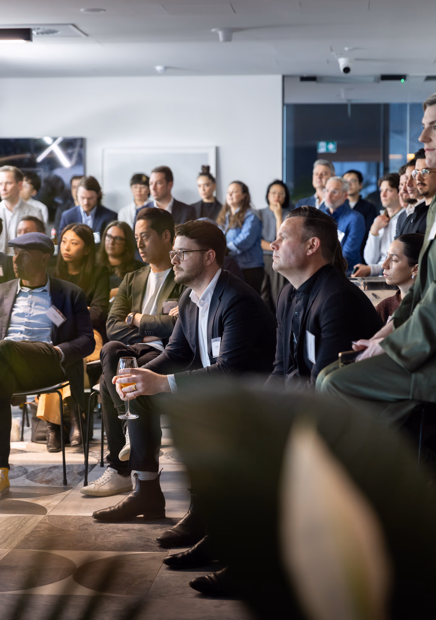 A seated audience in business attire listens intently at a Fraser & Partners event in an office space.