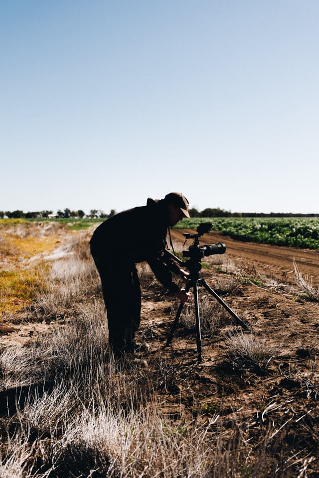 A videographer silhouetted against the sky sets up a camera on a tripod beside a Providore Global farm field.