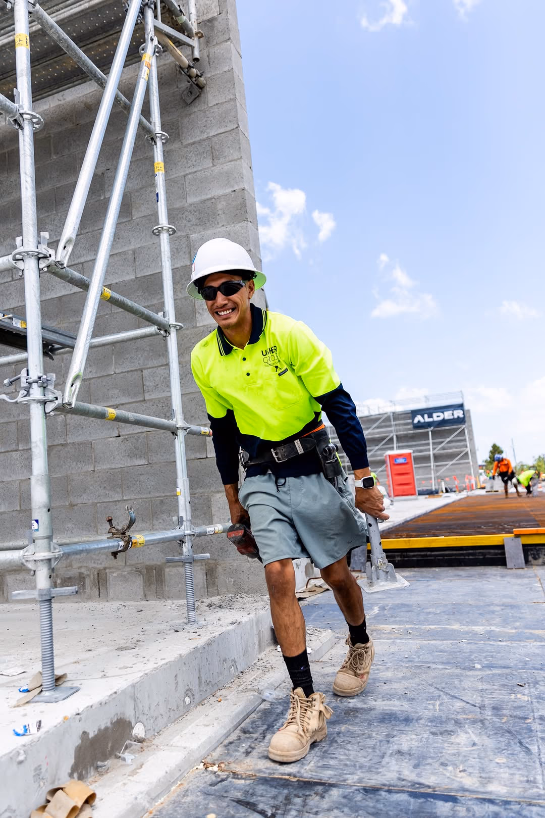 A Usher Group construction worker in hi-vis and a hard hat smiles while working on scaffolding.