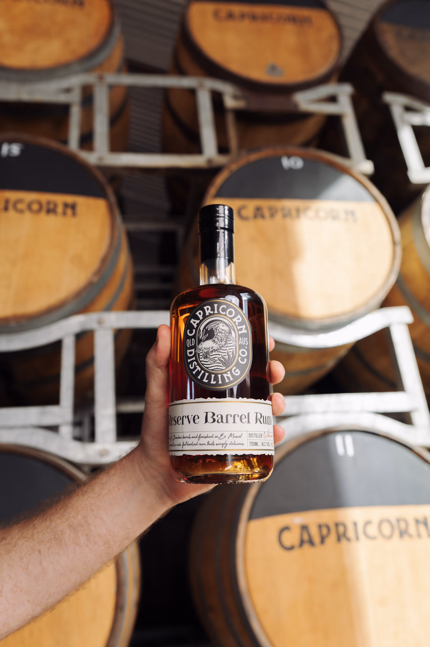 A bottle of Capricorn Reserve Barrel Rum held in front of the barrel racks