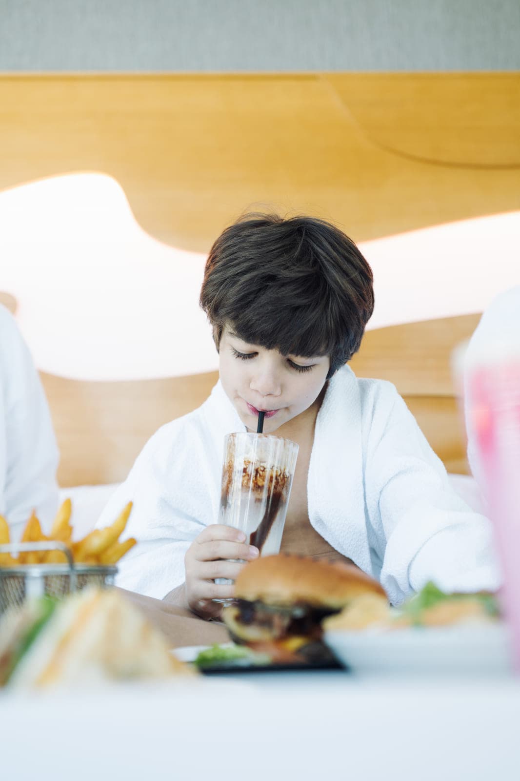 A child in a hotel robe with a milkshake and burger from room service